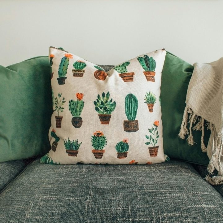 A modern living room with green cushions, cactus pillow, and cozy throw blanket on a sofa.