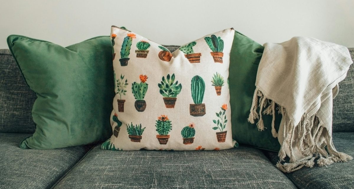 A modern living room with green cushions, cactus pillow, and cozy throw blanket on a sofa.